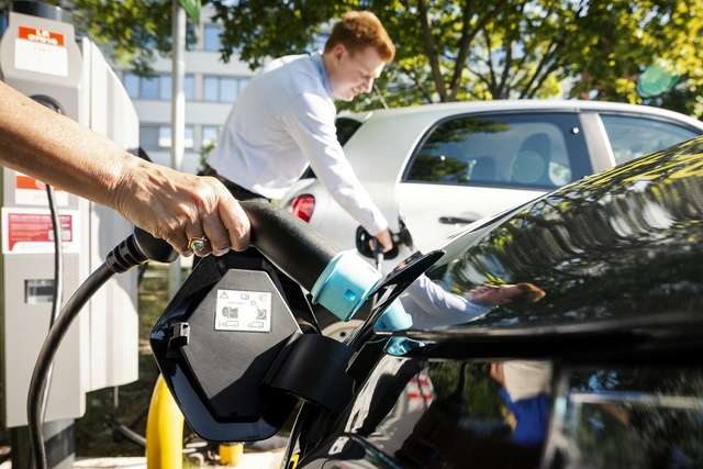 Das Foto zeigt eine Hand im Vordergrund, die einen Ladestecker ins E-Auto steckt