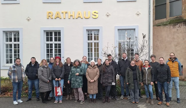 Eine Menschengruppe steht vor einem Haus und schaut in die Kamera