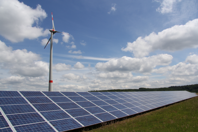 Freiflächen-Photovoltaik mit Windrad im Hintergrund