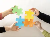 vier Hände setzen Puzzle-Teile zusammen