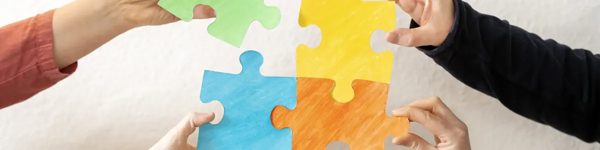 vier Hände setzen Puzzle-Teile zusammen