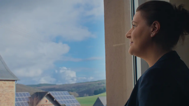 Eine Frau blickt aus dem Fenster auf Hausdächer mit PV
