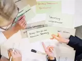 Drei Personen zeigen sich beschriftete Moderationskarten zum Thema Klimaschutz