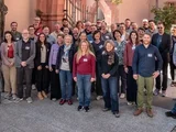 Viele Menschen stehen vor einem Gebäude und schauen in die Kamera