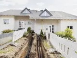 Blick auf zwei Häuser bei denen gerade in Nahwärmeanschluss verlegt ist. Der Boden ist noch offen und die Rohre, die zu den Häusern führen, sind zu sehen.