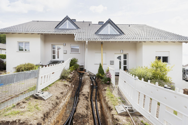 Blick auf zwei Häuser bei denen gerade in Nahwärmeanschluss verlegt ist. Der Boden ist noch offen und die Rohre, die zu den Häusern führen, sind zu sehen.
