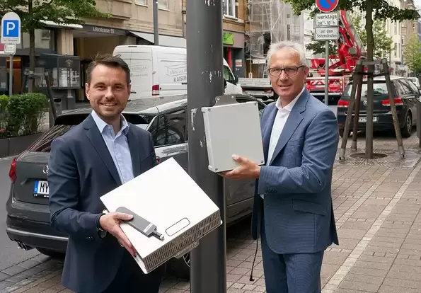 Oberbürgermeister David Langner (links) und evm-Vorstandsvorsitzender Josef Rönz zeigen die Luftsensoren, die an Laternenmasten entlang der Löhrstraße montiert sind