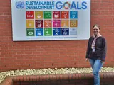 Frau steht vor einer Hauswand, an der eine Tafel mit Nachhaltigkeitszielen hängt