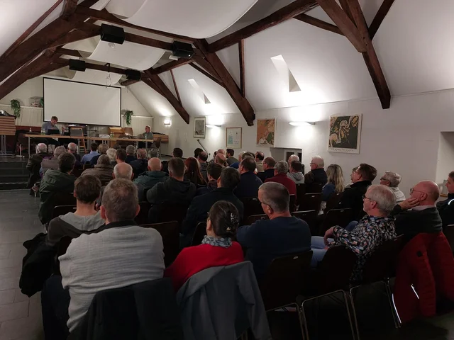 Viele Menschen sitzen in Reihen in einem Raum und hören einem Redner zu