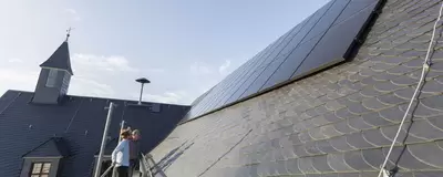 Photovoltaik-Elemente auf einem Dach eines kommunalen Gebäudes, daneben ein Kirchturm.