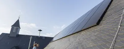 Photovoltaik-Elemente auf einem Dach eines kommunalen Gebäudes, daneben ein Kirchturm.