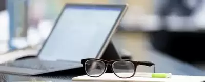 Aufgeklappter Laptop steht auf einem Tisch. Davor liegt eine Brille.