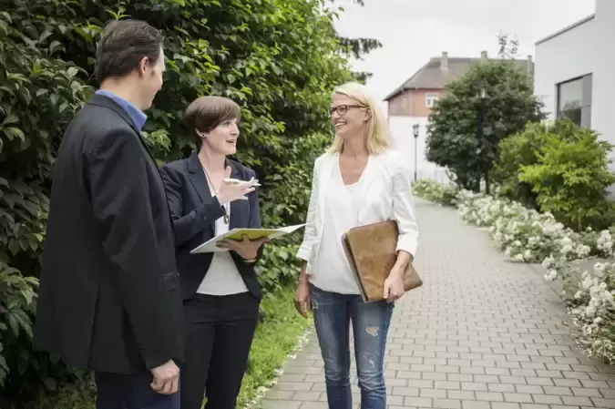 Drei Personen stehen auf einem Weg im Freien und besprechen etwas.