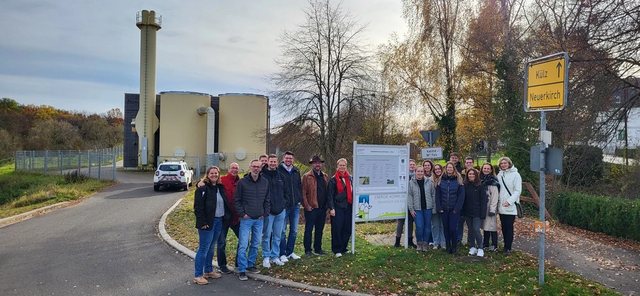 Mehrere Personen stehen um ein Schild herum und schauen in die Kamera