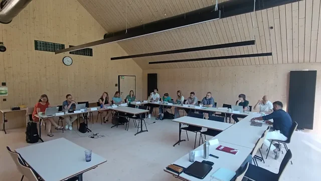 Mehrere Menschen sitzen an Tischen in einem großen, hellen Saal