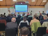 Viele Menschen sitzen in einem Raum und schauen sich eine Präsentation auf einem großen Bildschirm an