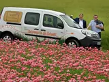 Zwei Personen vor dem E-Carsharing-Auto im Blumenfeld
