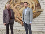 Zwei Männer stehen vor einer Mauer und schauen in die Kamera