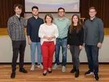 Sechs Personen stehen vor einer Leinwand und schauen in die Kamera