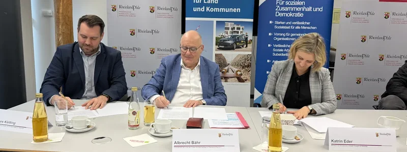 Zwei Männer und eine Frau sitzen an einem Tisch und unterschreiben alle ein Dokument