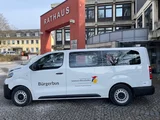 Ein Weißer neuer Kleinbus parkt vor einem Rathaus