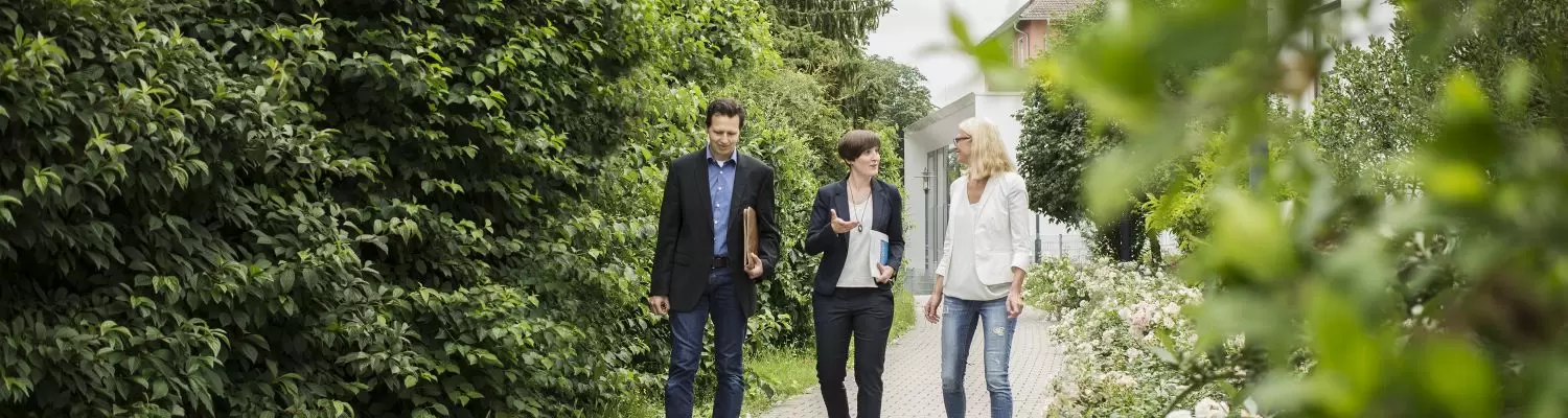 Drei Menschen laufen einen Weg entlang und unterhalten sich. Symbolbild Beratung.