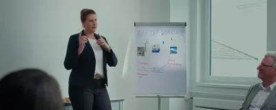 Eine Frau steht neben einem Flip Chart und erklärt etwas. Auf dem Flipchart steht "Kick off Workshop".