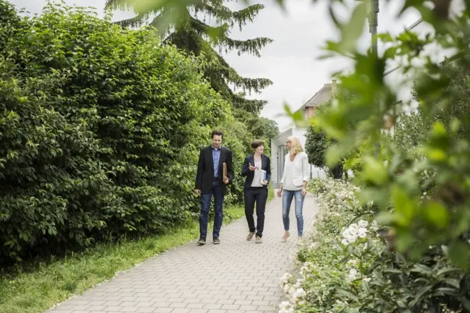 Drei Personen gehen einen Weg entlang im Freien und besprechen etwas.