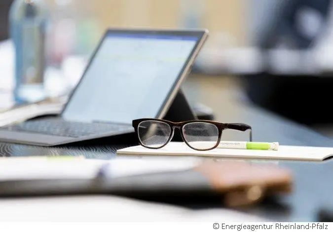 Laptop, Brille und Schreibunterlagen liegen auf einem Tisch