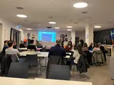 Mehrere Menschen sitzen in einem Raum und hören einem Redner zu