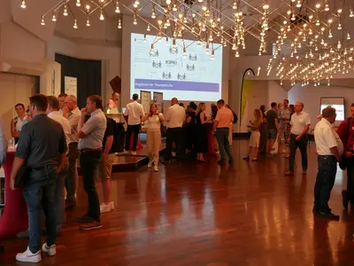 Viele Personen stehen in Gruppen in einem Raum und unterhalten sich