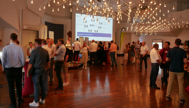 Viele Personen stehen in Gruppen in einem Raum und unterhalten sich