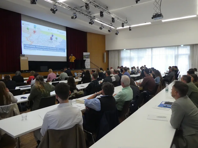 Viele Menschen sitzen an Tischen und schauen auf eine Präsentation