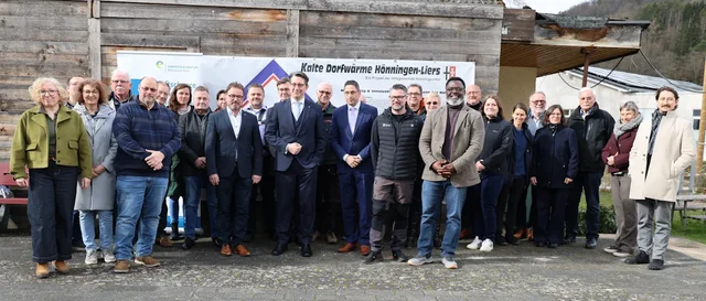 Viele Menschen stehen vor einem Plakat und sehen in die Kamera