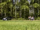 Das Foto zeigt ein E-Auto und eine Familie im Grünen