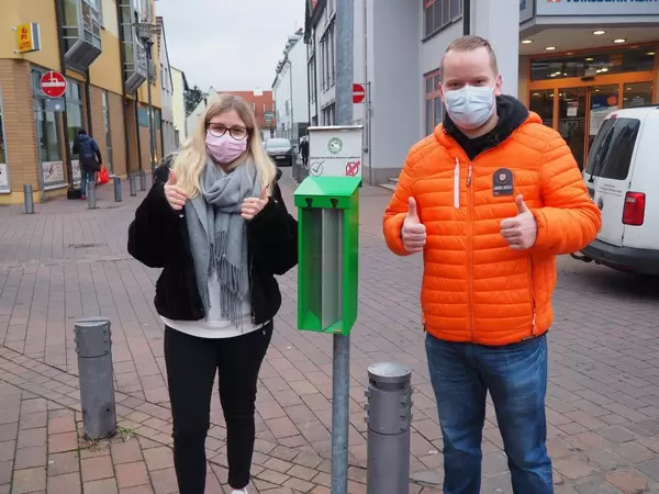 Zwei junge Personen zeigen Daumen hoch vor öffentlichem Ascher