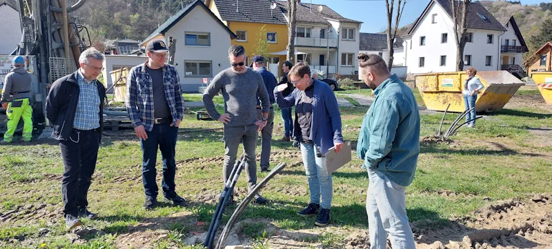 Mehrere Menschen stehen auf einer Wiese und schauen auf Leitungen, die aus der Erde ragen