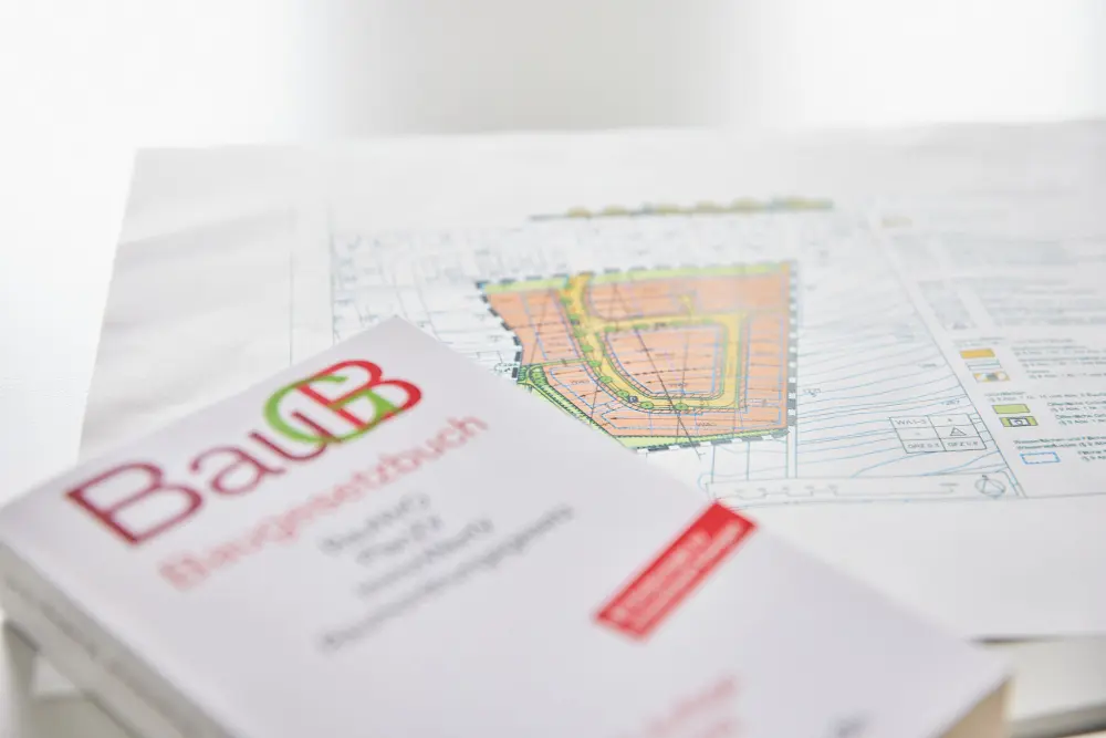 Auf dem Tisch liegt ein Plan, daneben liegt das Baugesetzbuch.