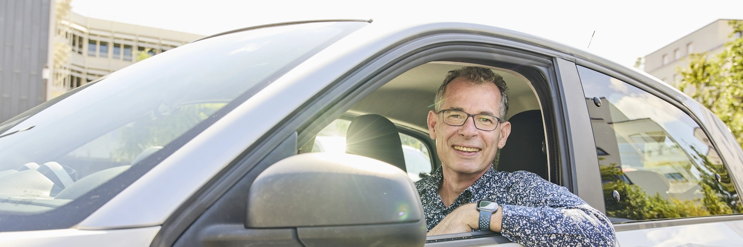 Der Projektleiter der Lotsenstelle für alternative Antriebe, Dr. Peter Götting, blickt lächelnd aus einem Elektroauto.
