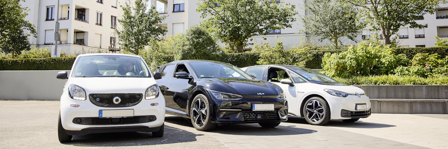 Drei verschiedene Modelle von Elektroautos stehen nebeneinander auf einem Platz